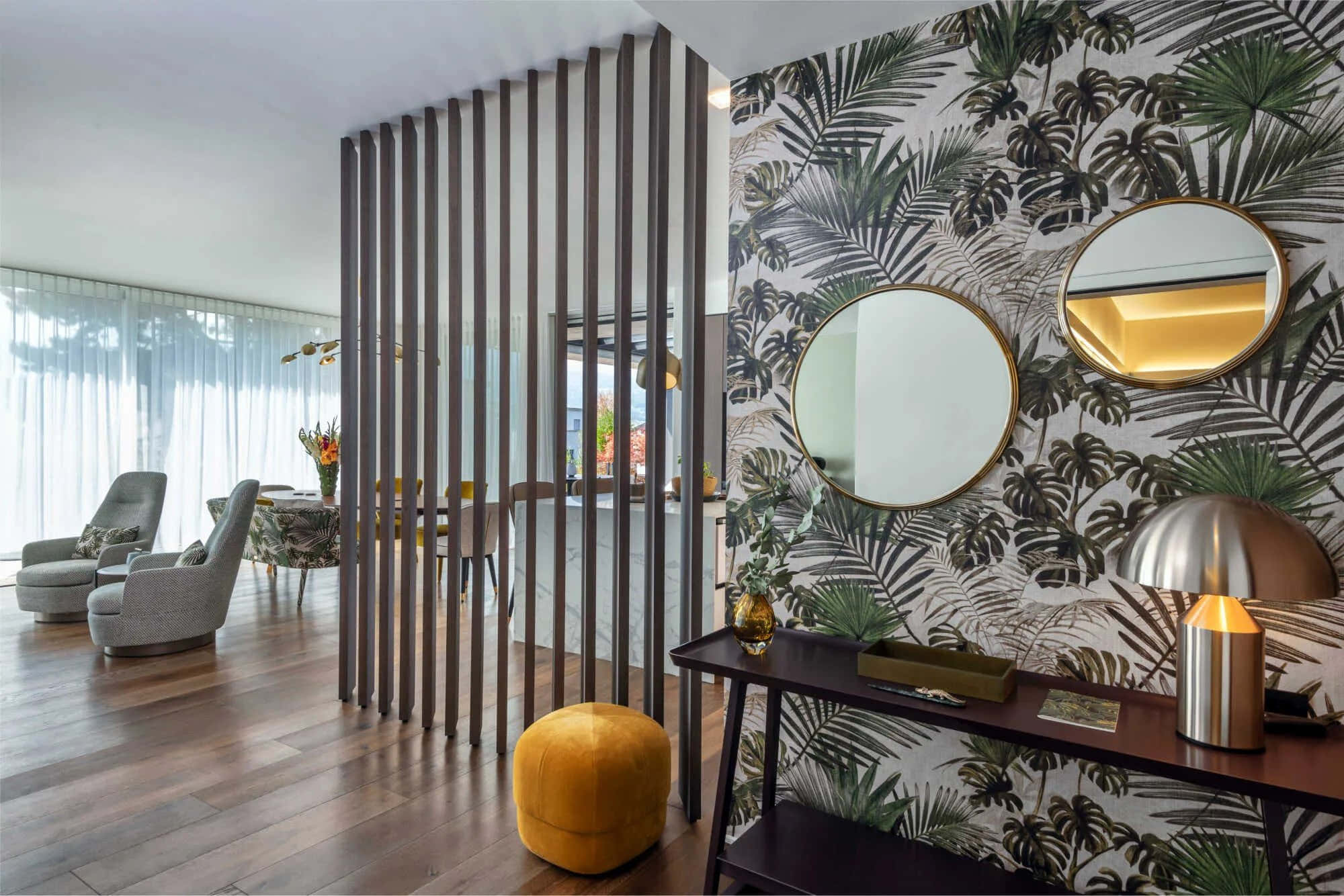 Creative Design Picture — Modern lounge with tropical leaf wallpaper, round mirrors, and a mustard ottoman under warm lighting.