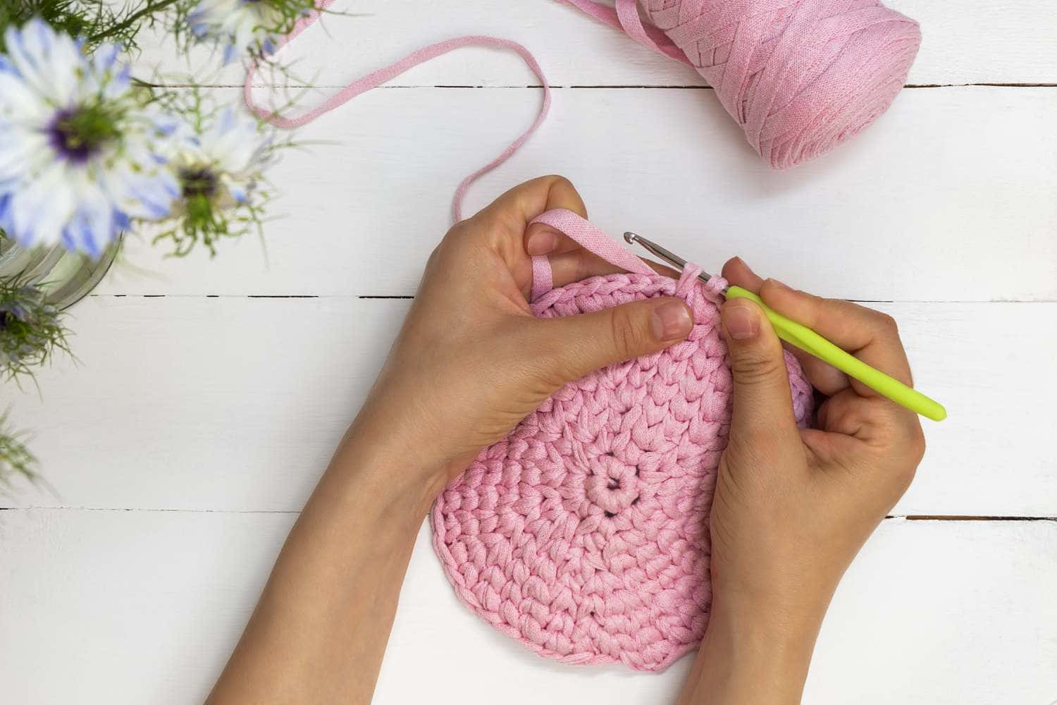 A Person Is Crocheting A Pink Crocheted Bag