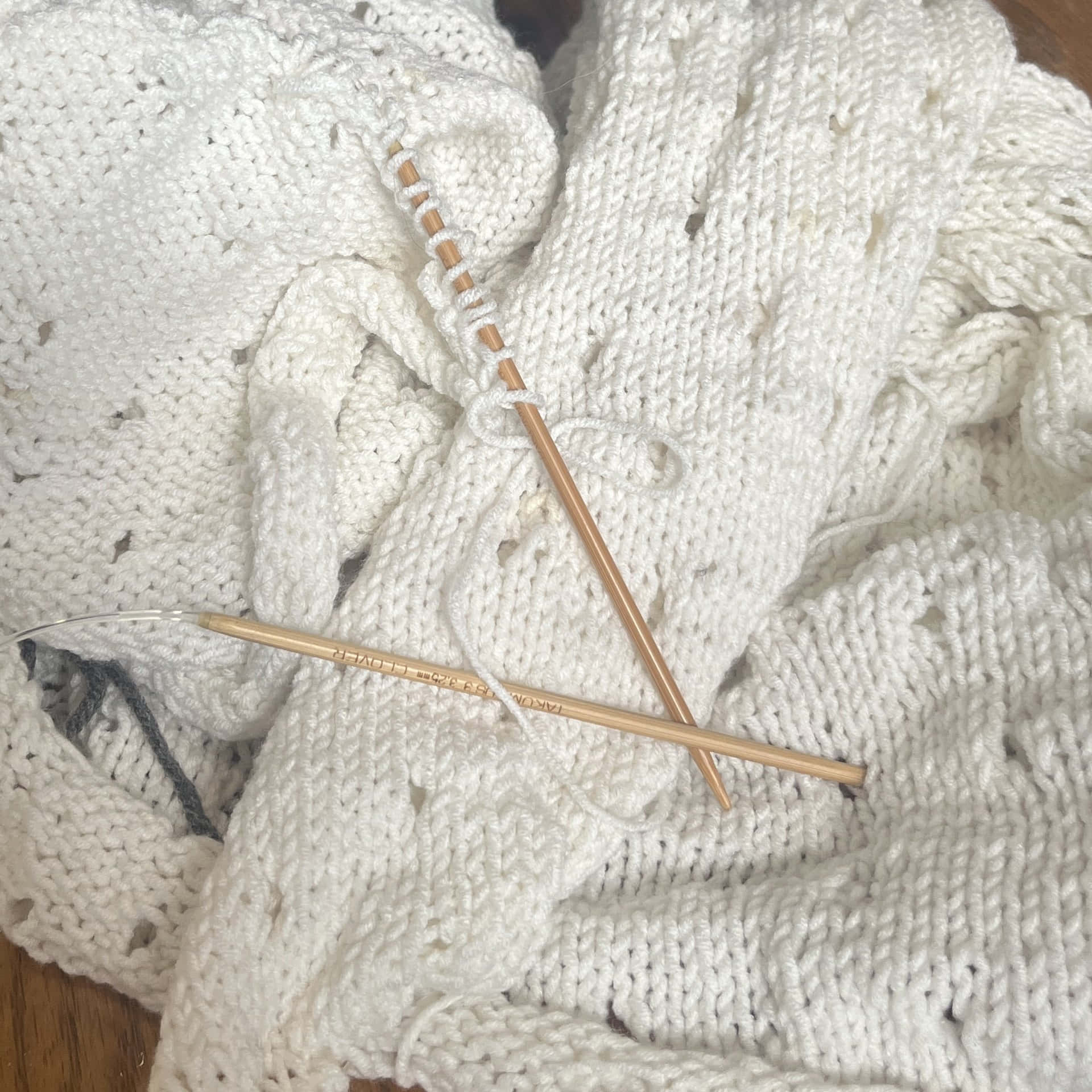 A White Knitted Sweater With Knitting Needles On Top