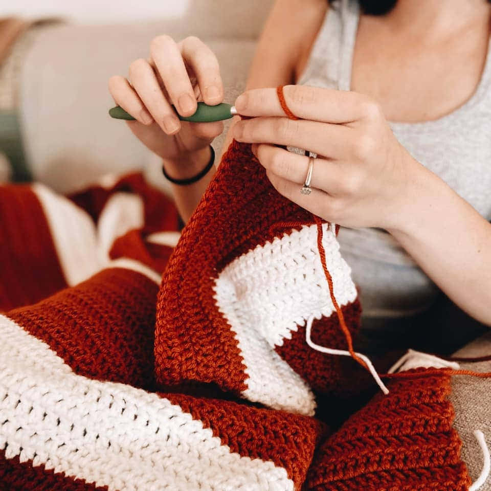A Woman Is Knitting A Blanket On A Couch