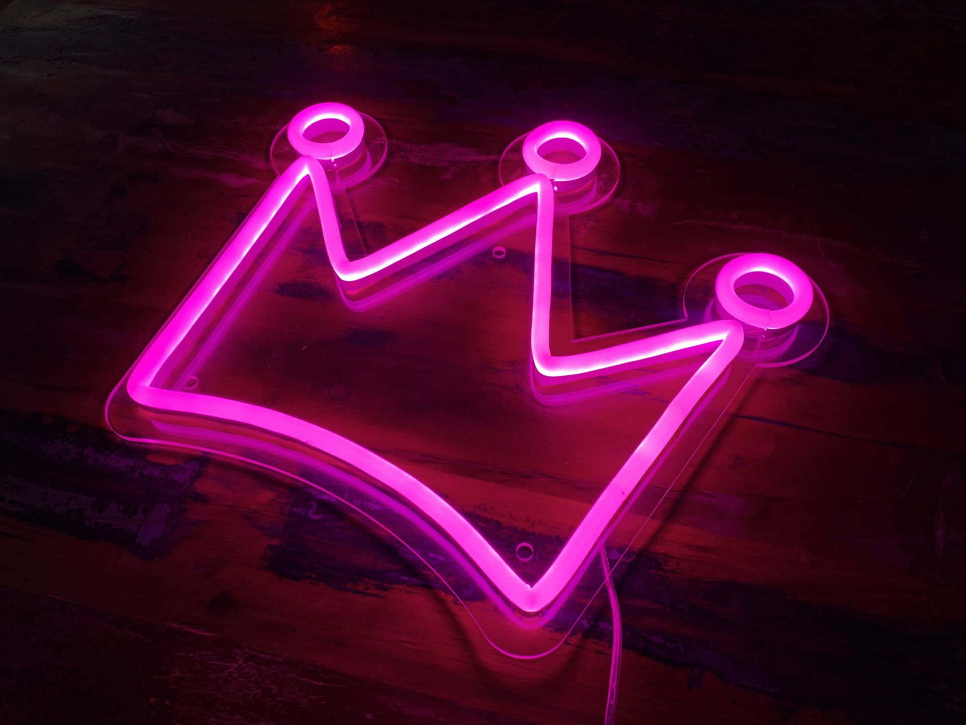 Download A Neon Crown Sign Is Lit Up On A Wooden Floor | Wallpapers.com