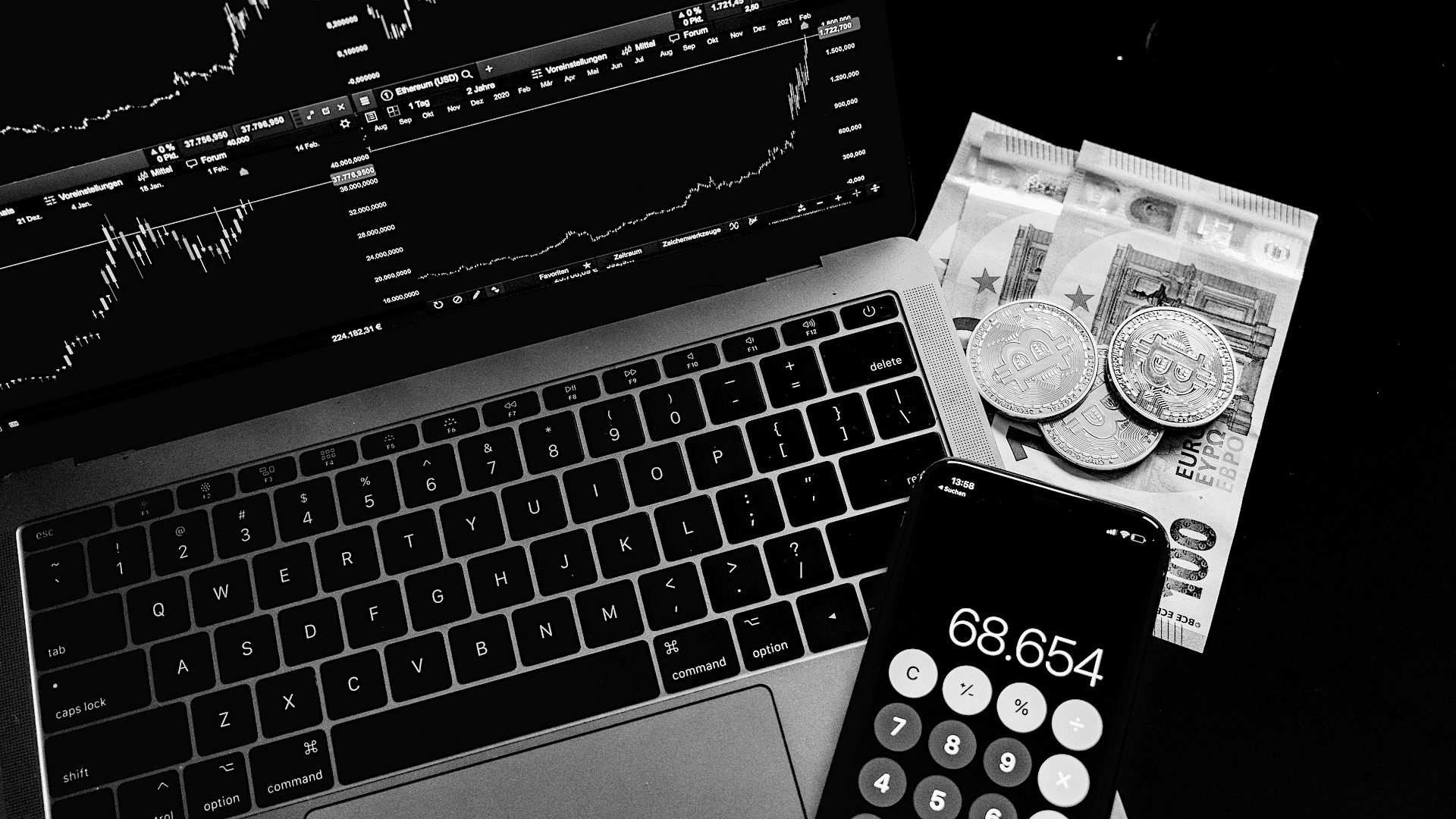 Crypto Background — Black and white close-up of a laptop displaying financial charts beside euro bills coins and a calculator showing 68.654.