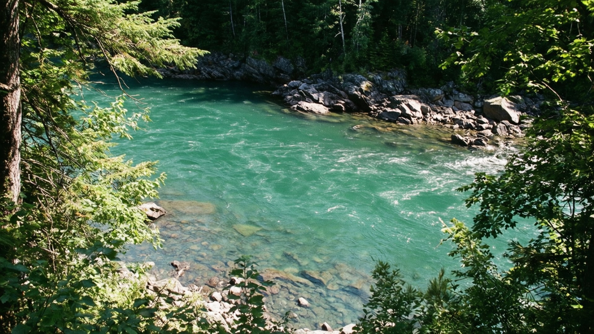 A clear turquoise river flows through a rocky forest with green trees. — Saguenay Picture