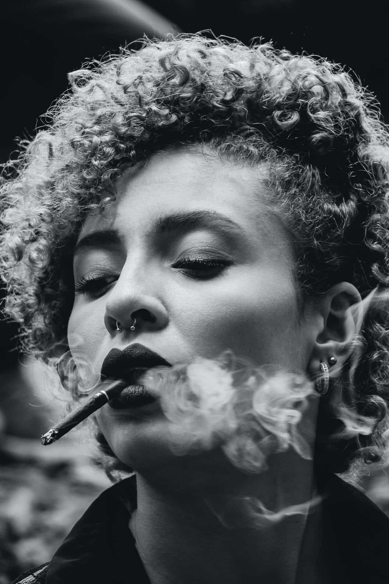 A carefree young woman with curly hair enjoying a serene moment with her cigarette Wallpaper