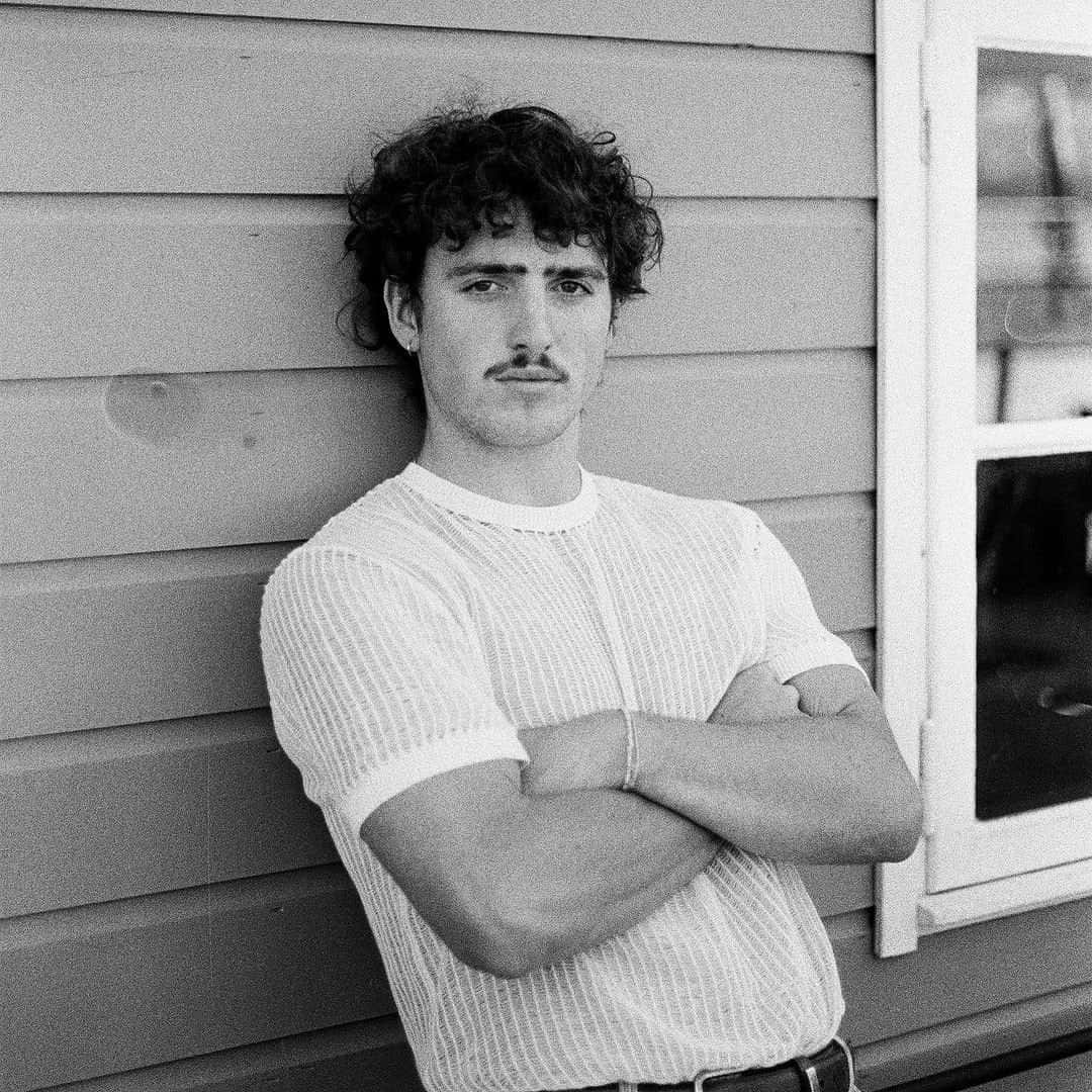 Curly Haired Man Leaning Against Wall Wallpaper