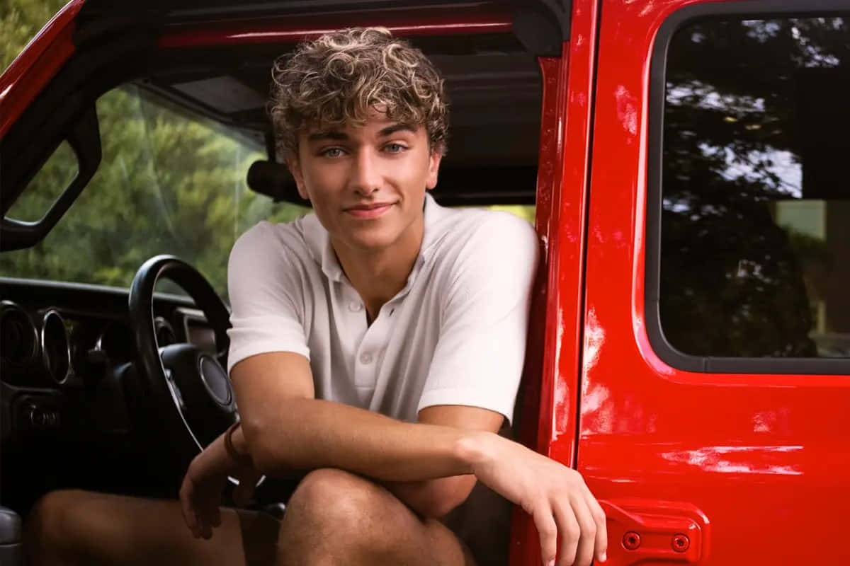 Curly Haired Teen Leaningon Red Car Wallpaper