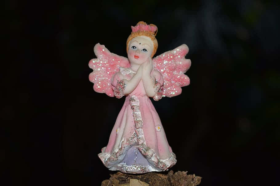 Endearing angel figurine with delicate pink wings Wallpaper