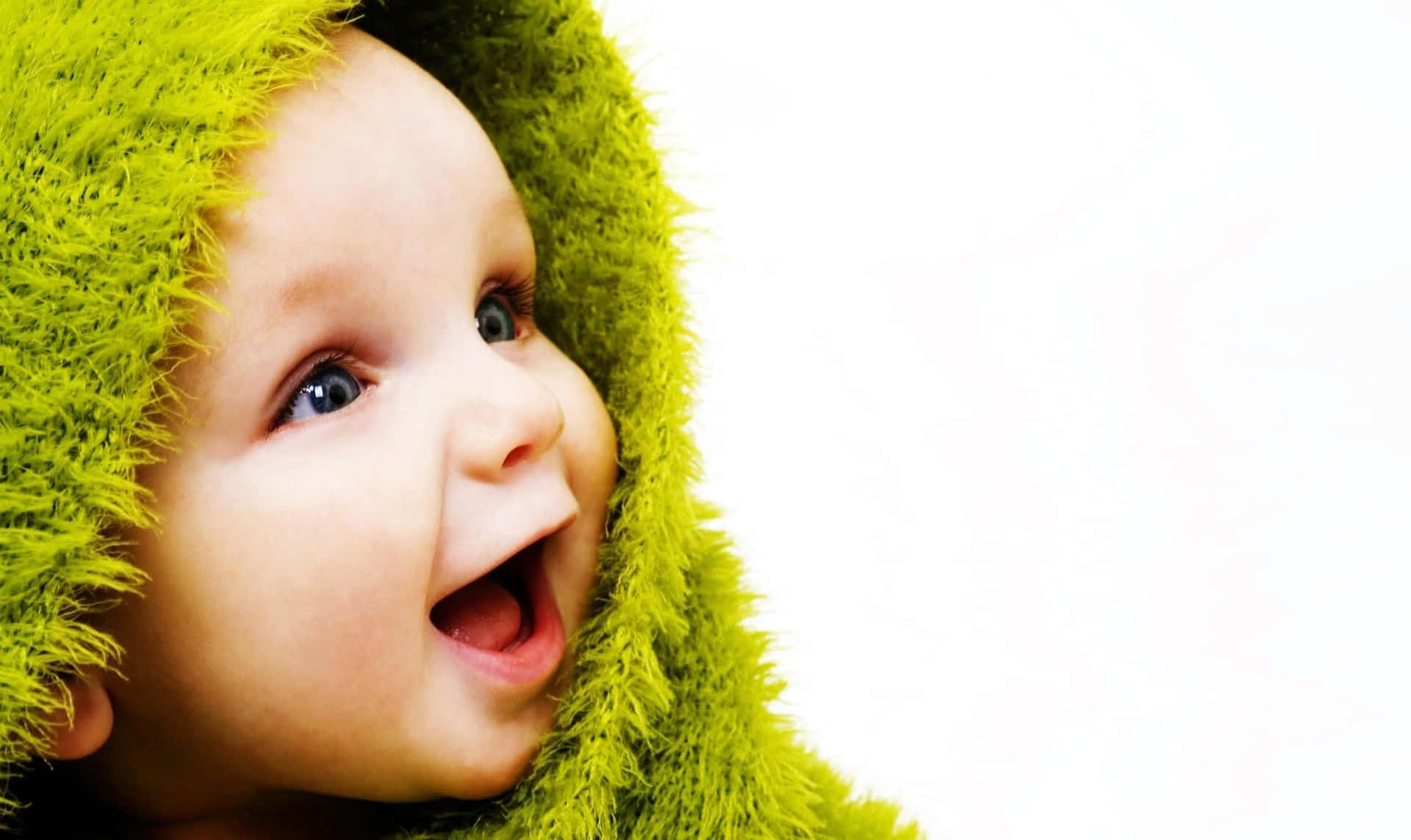 A Baby In A Green Furry Blanket Is Laughing