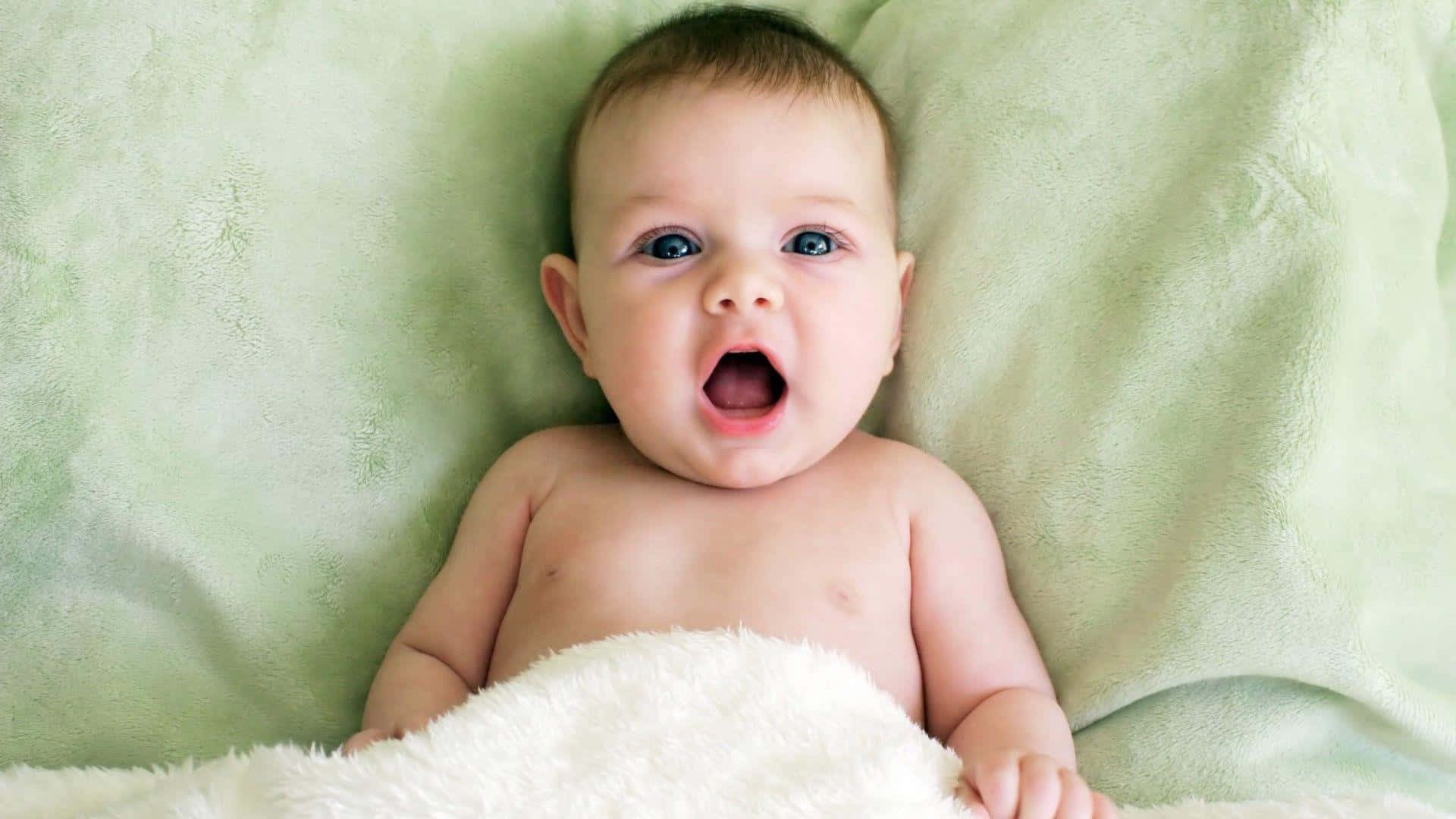 A Baby Is Laying On A Green Blanket With Its Mouth Open