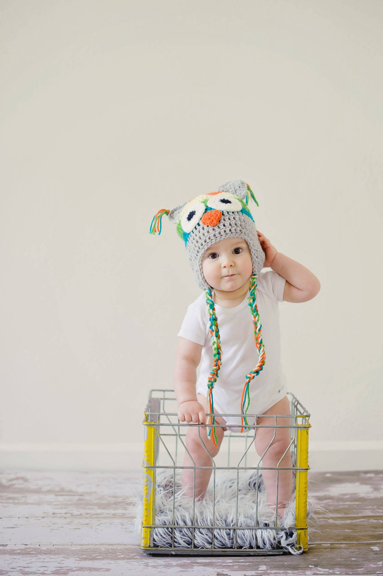 Adorable Baby Wearing an Owl Bonnet In a Crate Wallpaper