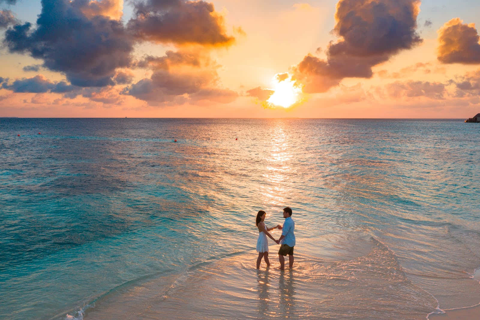 Couple Standing On The Beach At Sunset Wallpaper