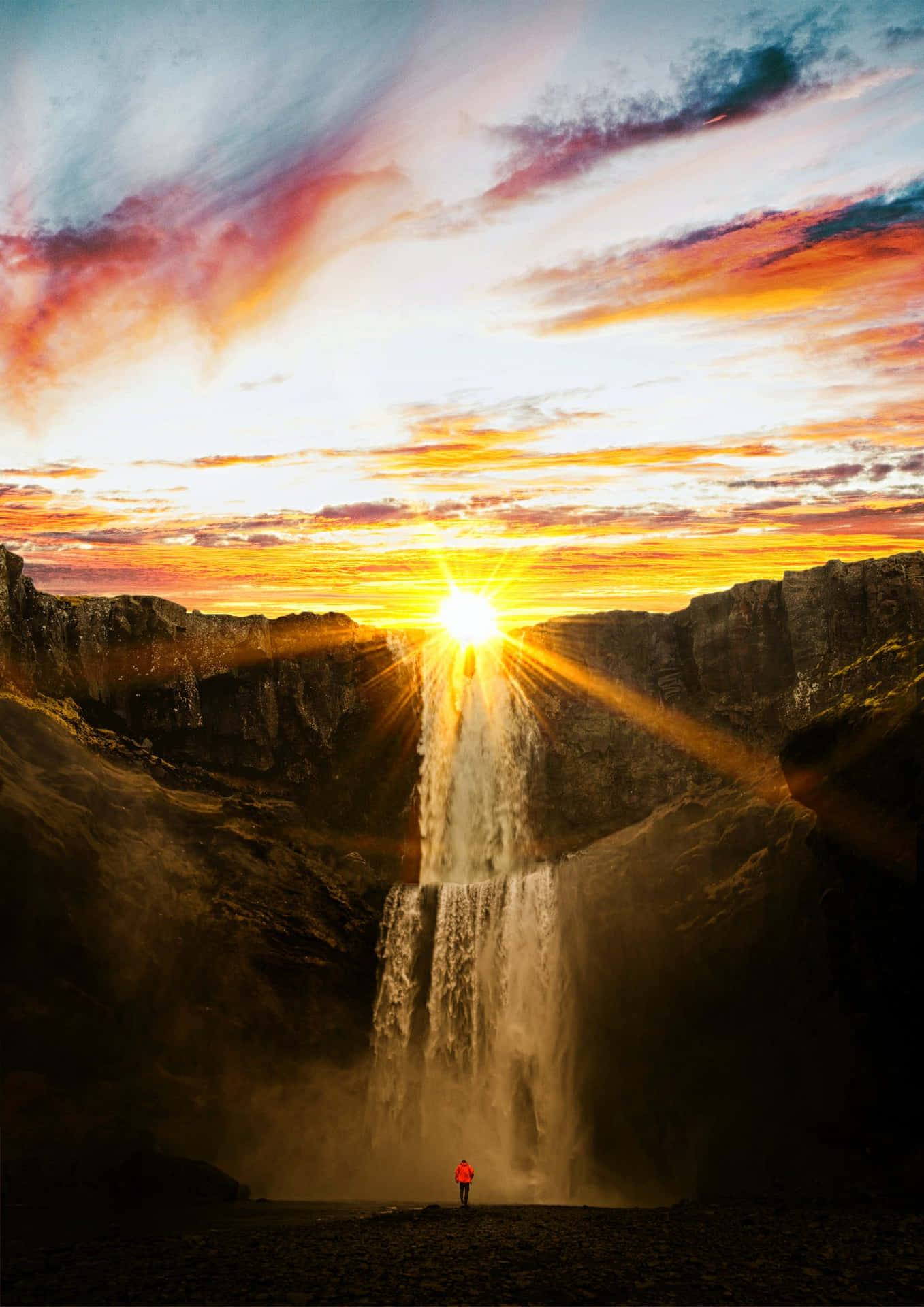 A Person Standing In Front Of A Waterfall At Sunset Wallpaper
