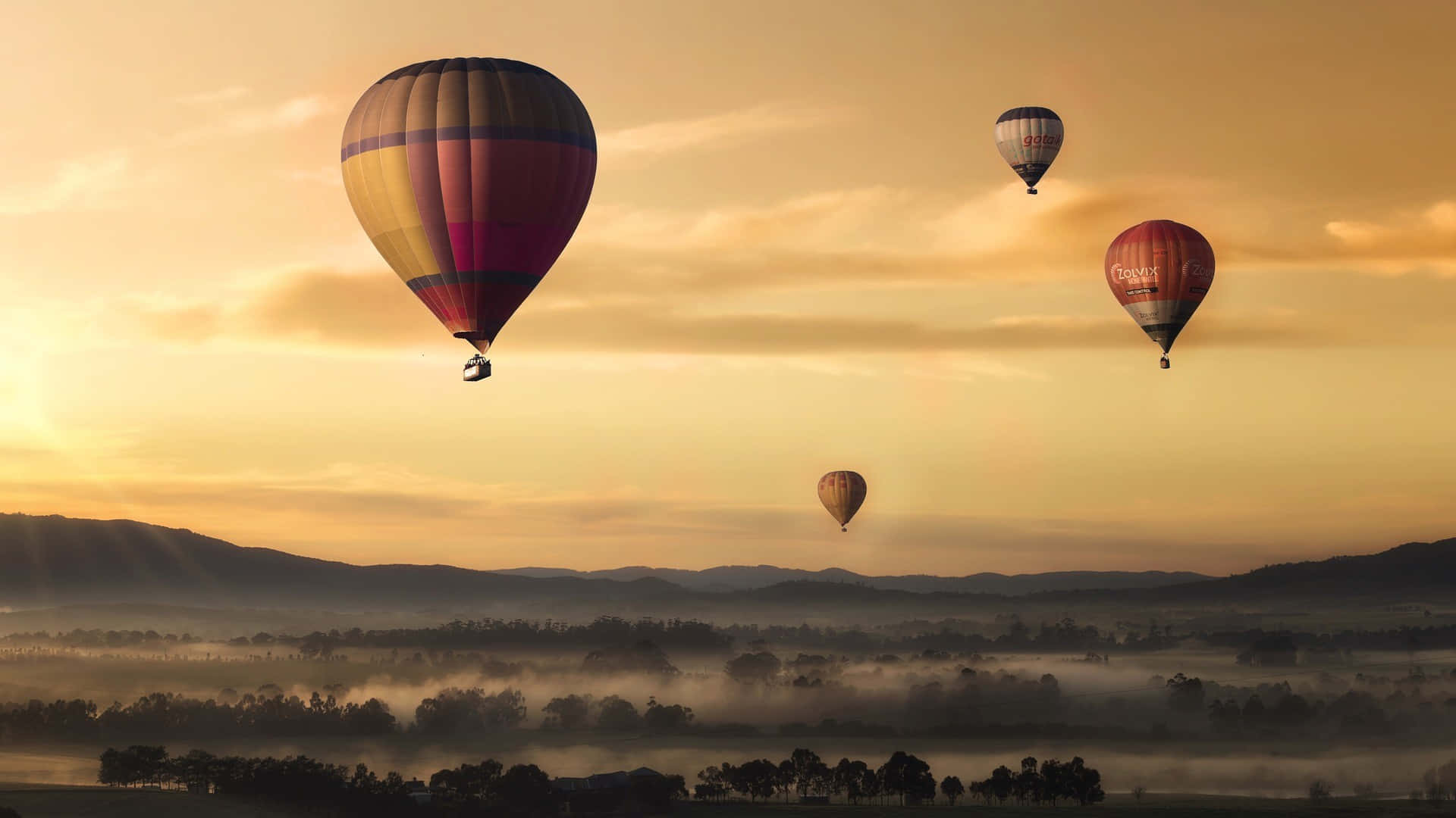 Heißluftballons,die Über Eine Nebelige Landschaft Fliegen. Wallpaper