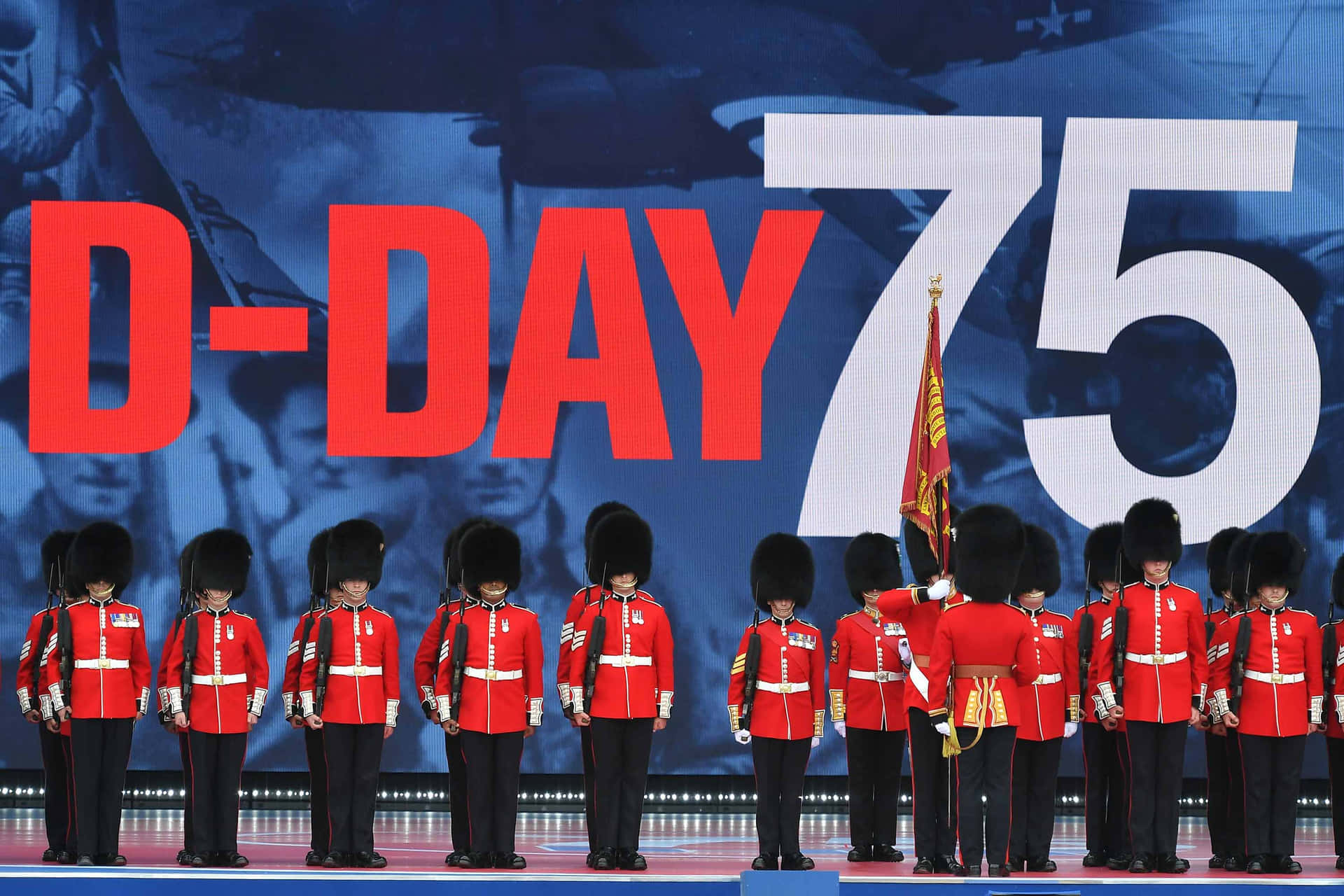 A Group Of Soldiers In Red Uniforms Standing In Front Of A Large Sign