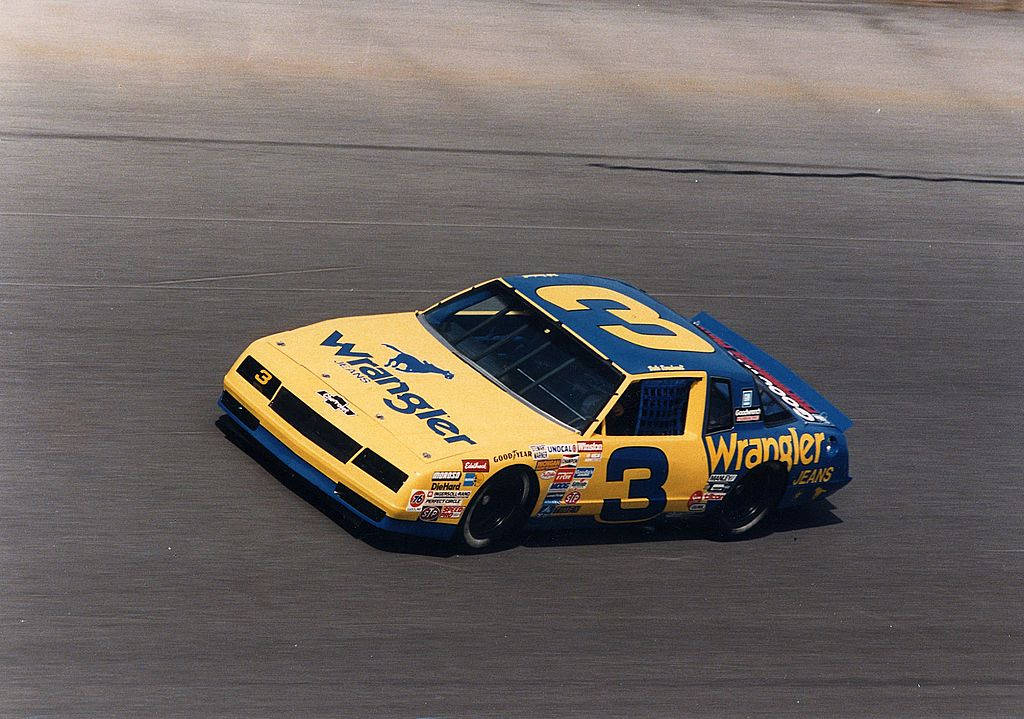 En gul og blå NASCAR-bil, der kører på en bane med stjerner i baggrunden. Wallpaper