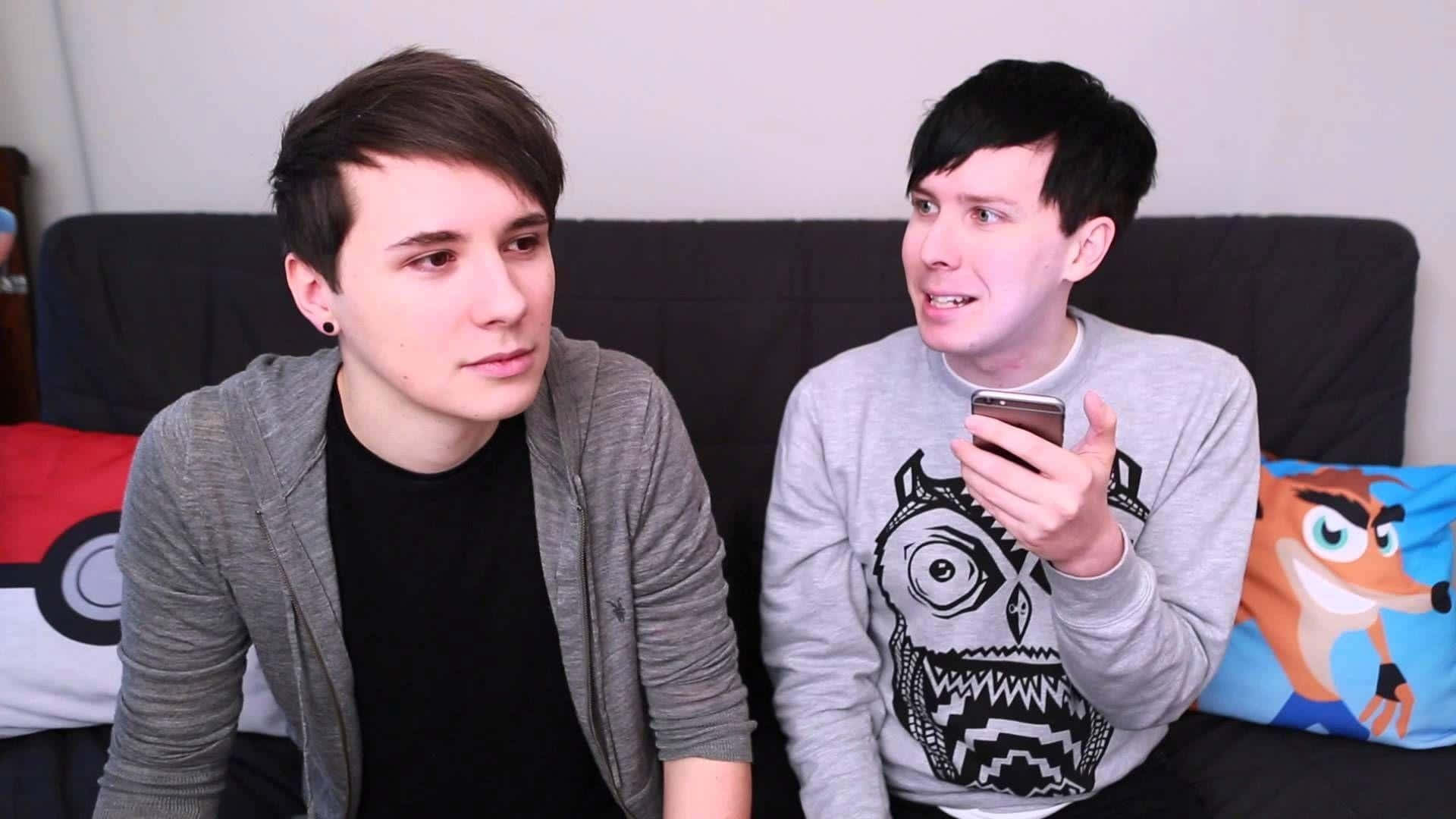 Dan og Phil sidder på en sofa ved siden af ​​en pejs Wallpaper