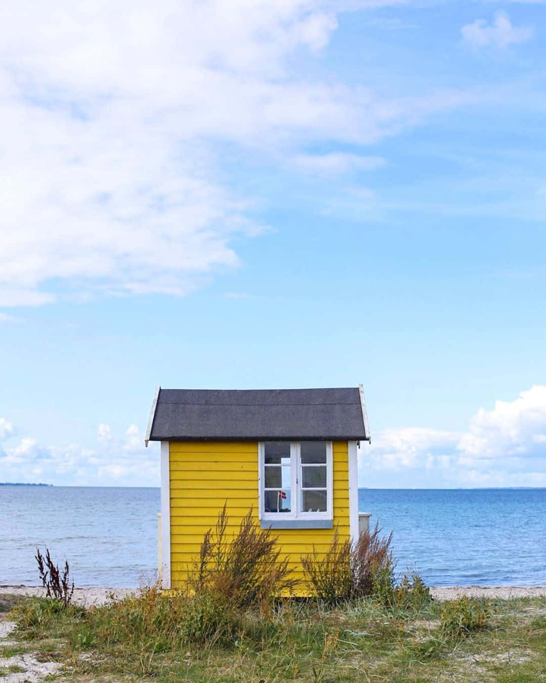 A Yellow Beach Hut Sits On The Shore Wallpaper