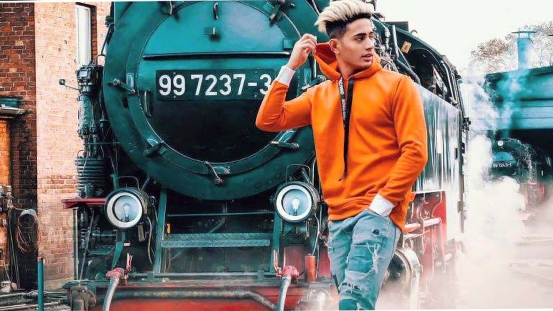 A Man In An Orange Hoodie Standing Next To A Train