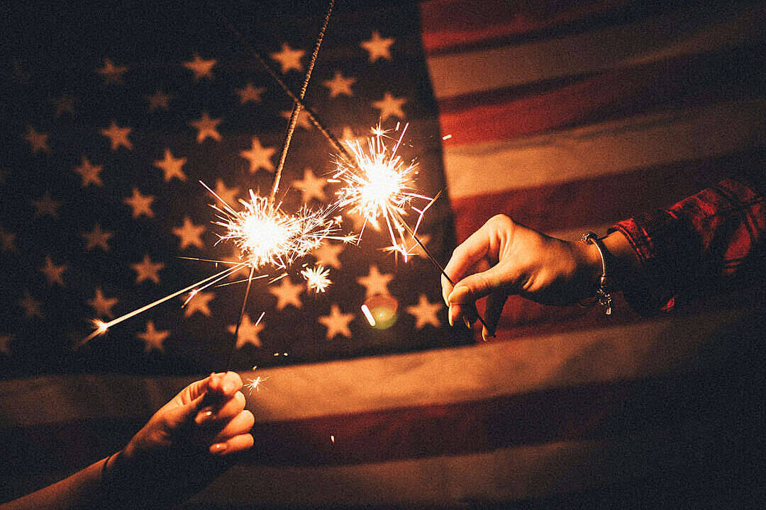 Dark American Flag Behind Two Hands Holding Sparklers Background