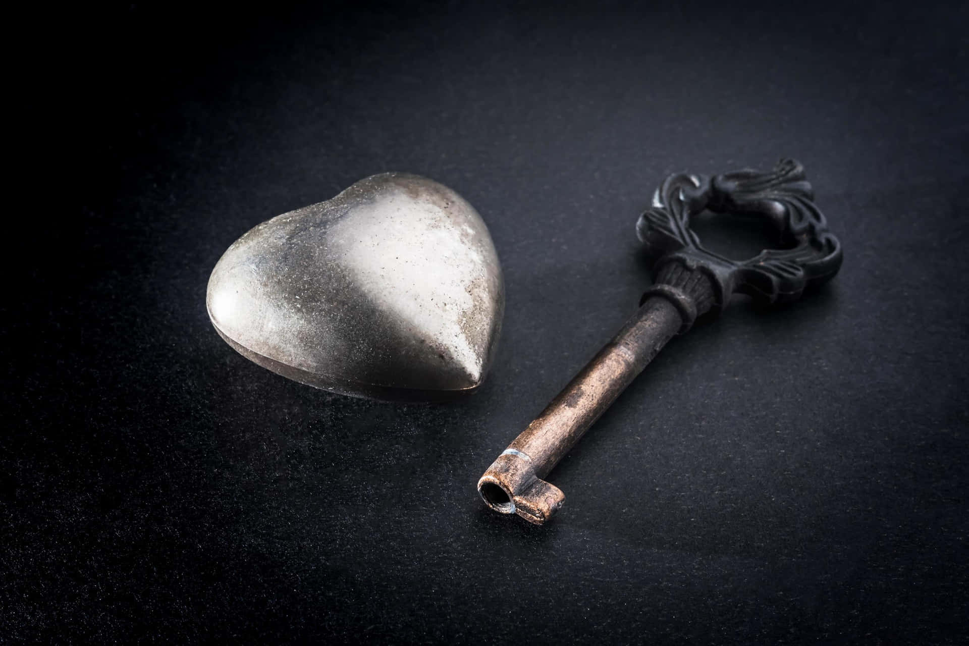a key and a heart shaped metal object on a black background