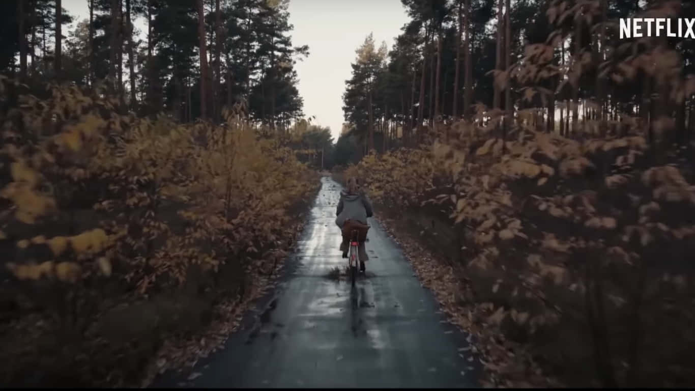 Enperson Åker Cykel Längs En Väg I Skogen Wallpaper