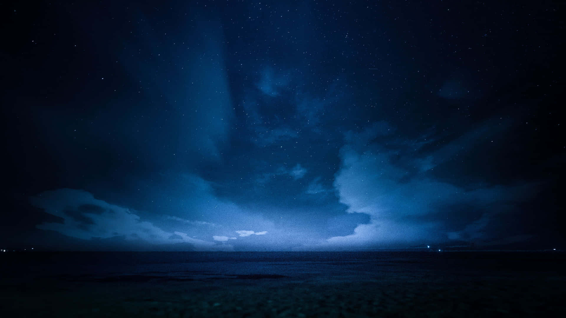 a blue sky with clouds and stars over the ocean