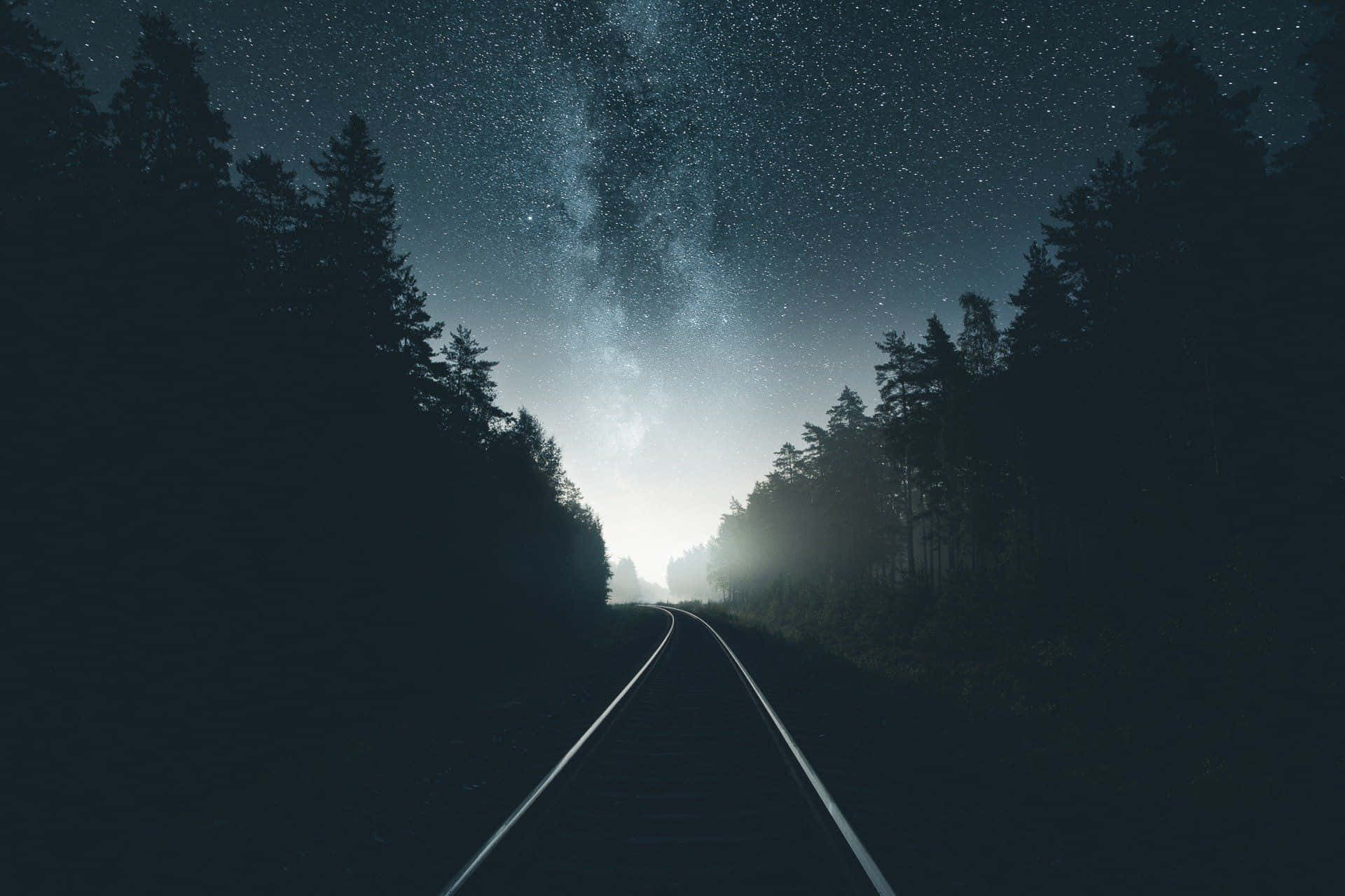 A Train Tracks In The Forest With The Stars Above Wallpaper