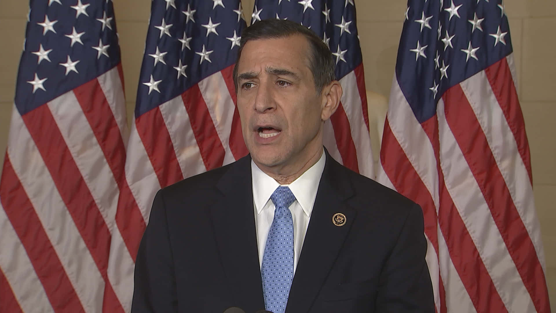 Darrell Issa Standing Proudly in Front of Four American Flags Wallpaper