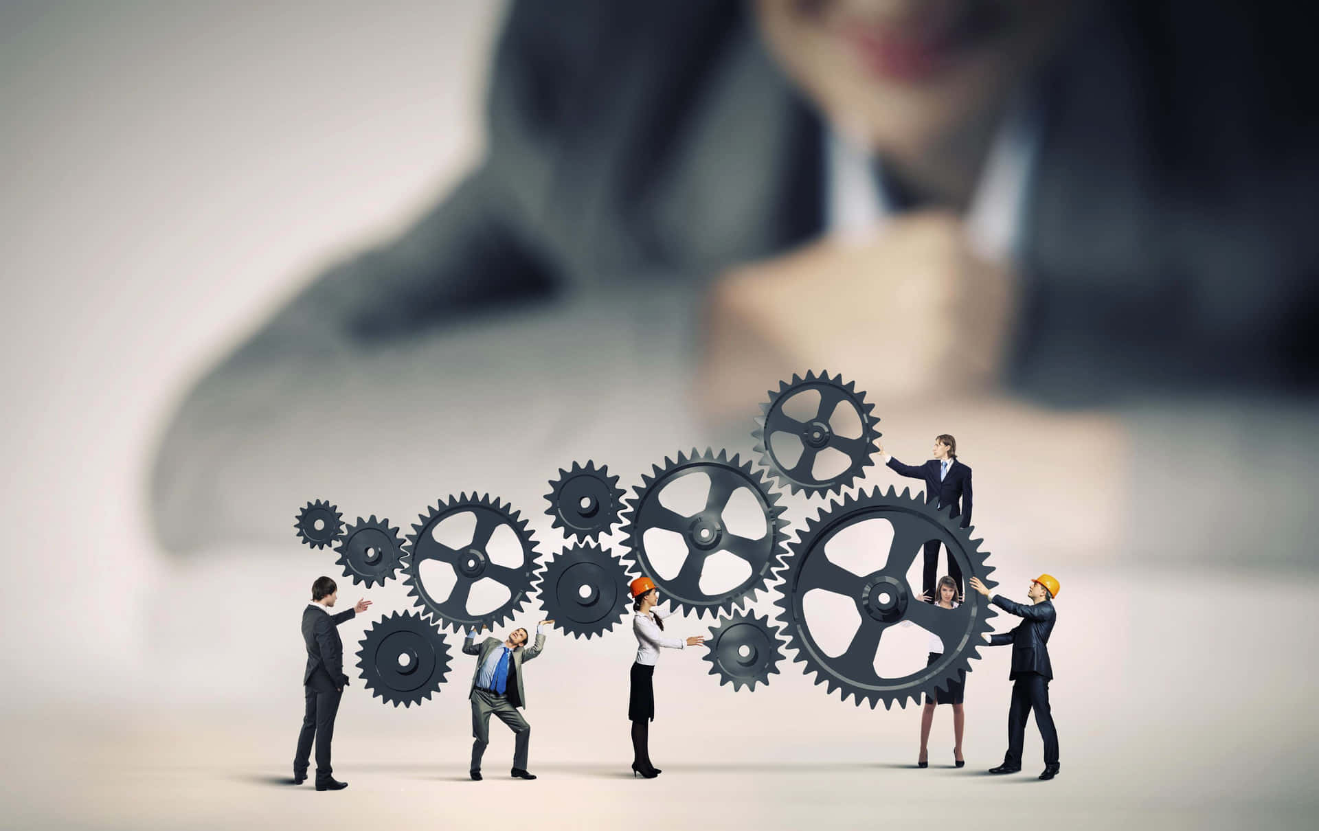 Data Effectively Managed Wallpaper — Tiny businesspeople assemble large black gears in front of a blurred corporate figure.