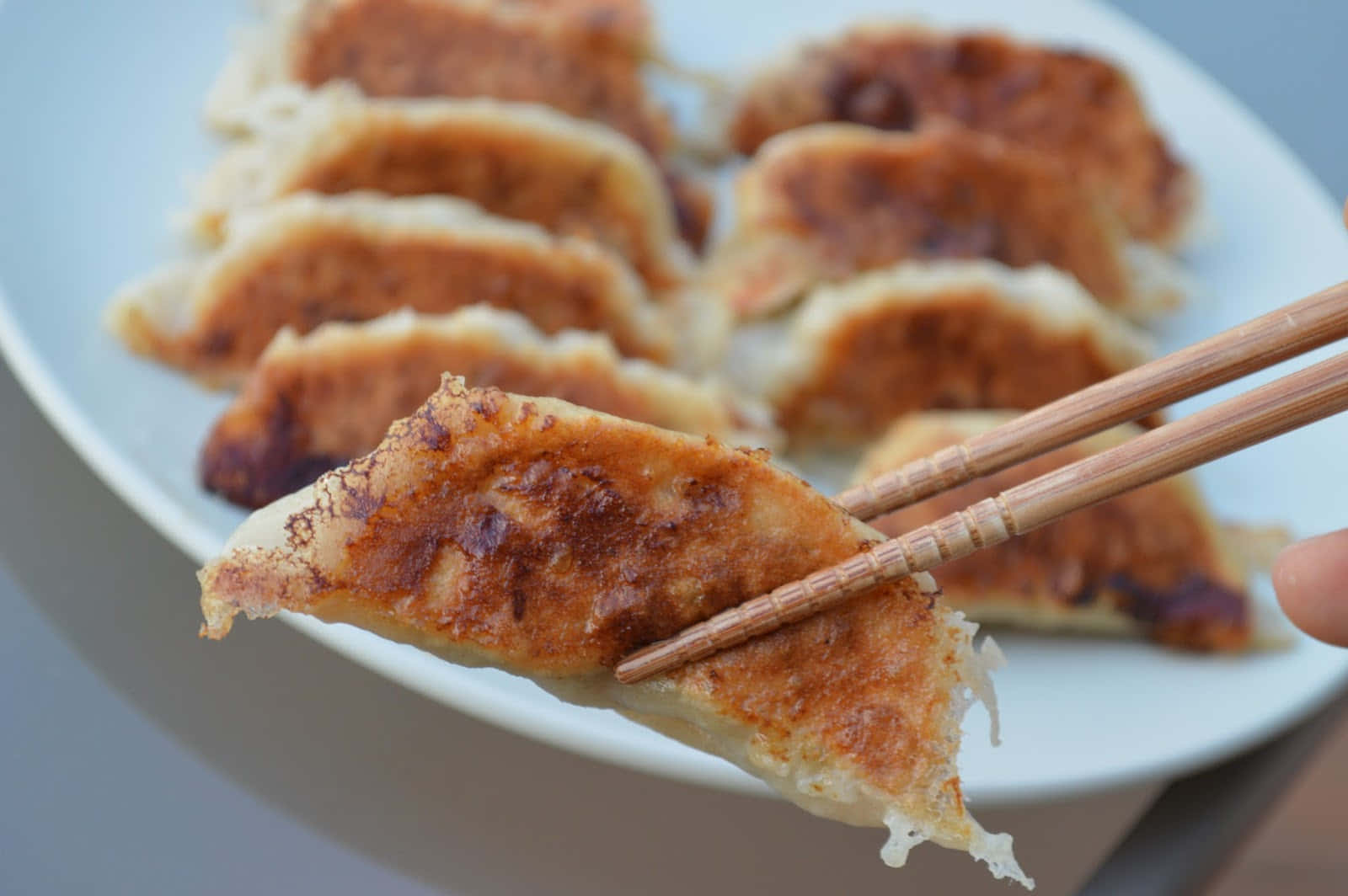 A Person Is Holding Chopsticks Over A Plate Of Dumplings