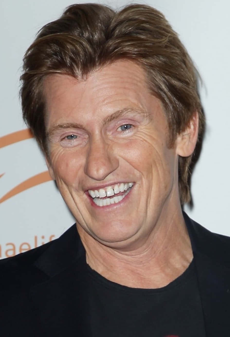 Comedian Denis Leary leaning on a brick wall Wallpaper