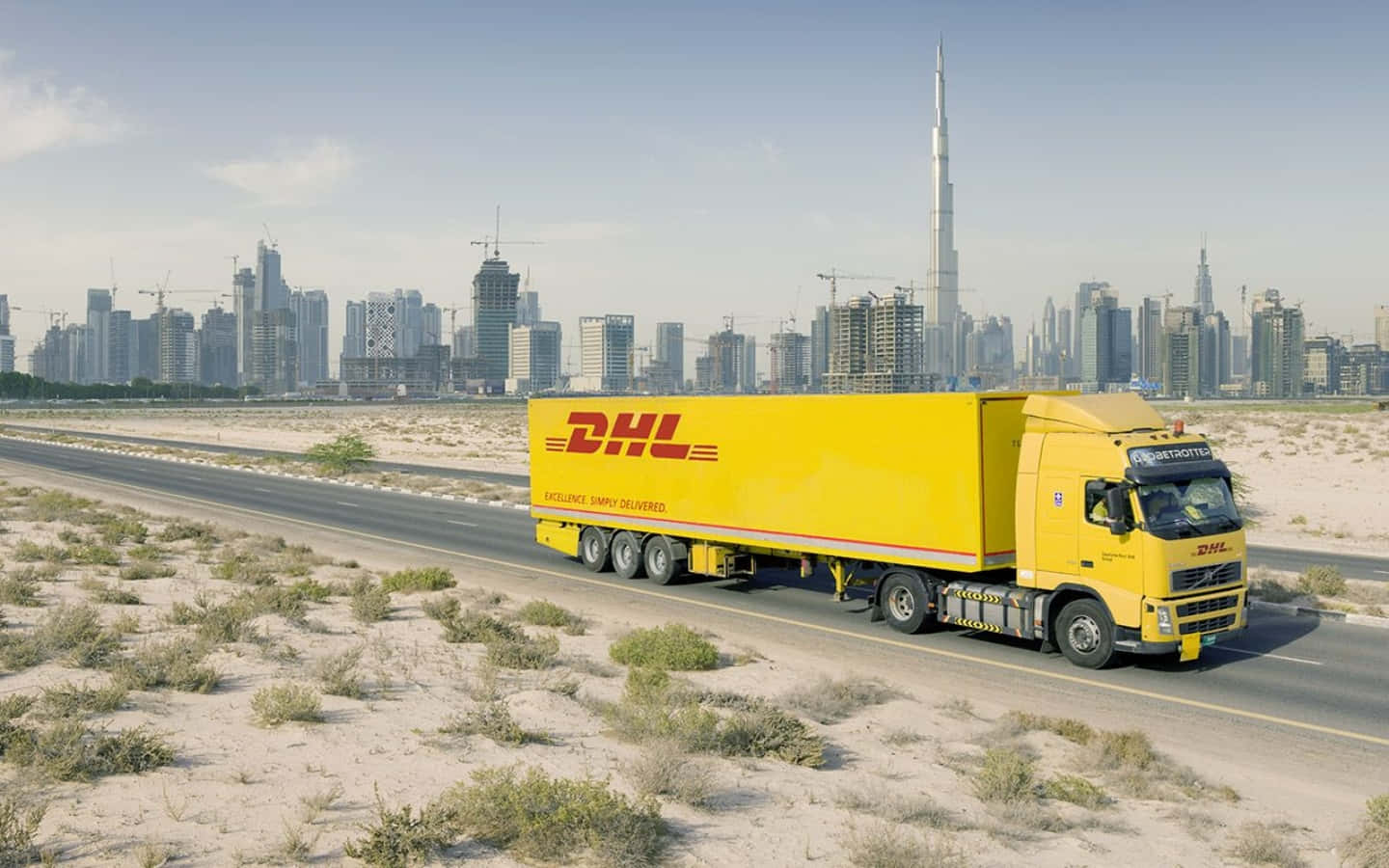Dhl Truck Driving Down The Road With A City In The Background