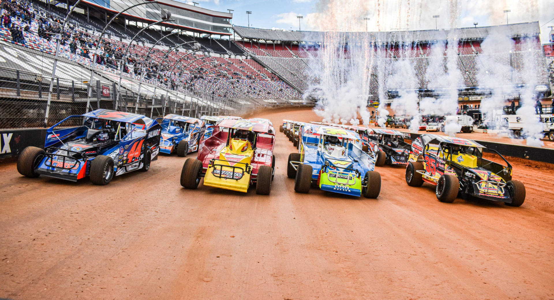 A Group Of Dirt Track Cars Driving In A Stadium Wallpaper