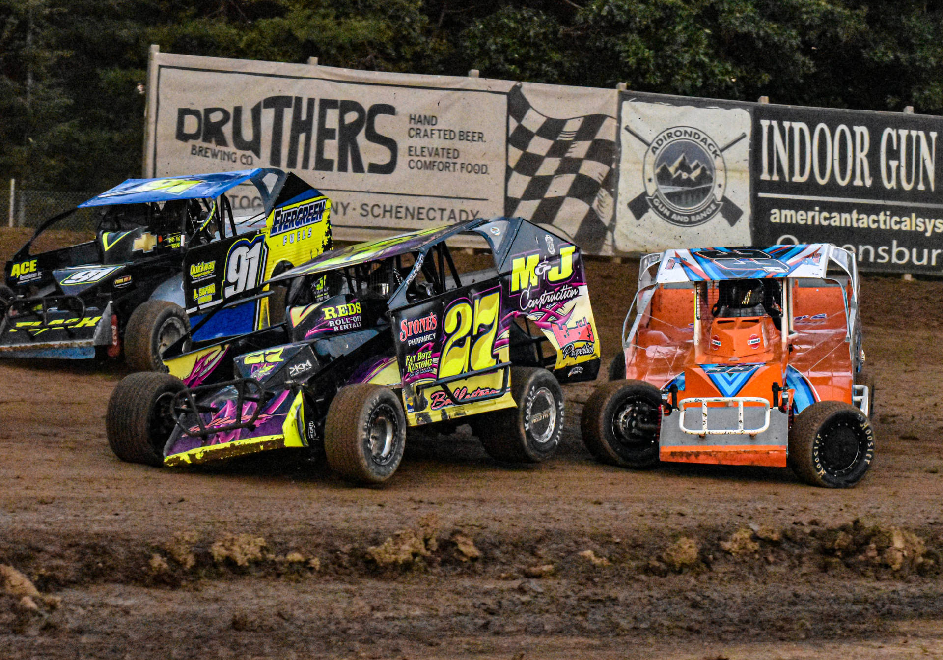 Three Dirt Cars Racing On A Dirt Track Wallpaper