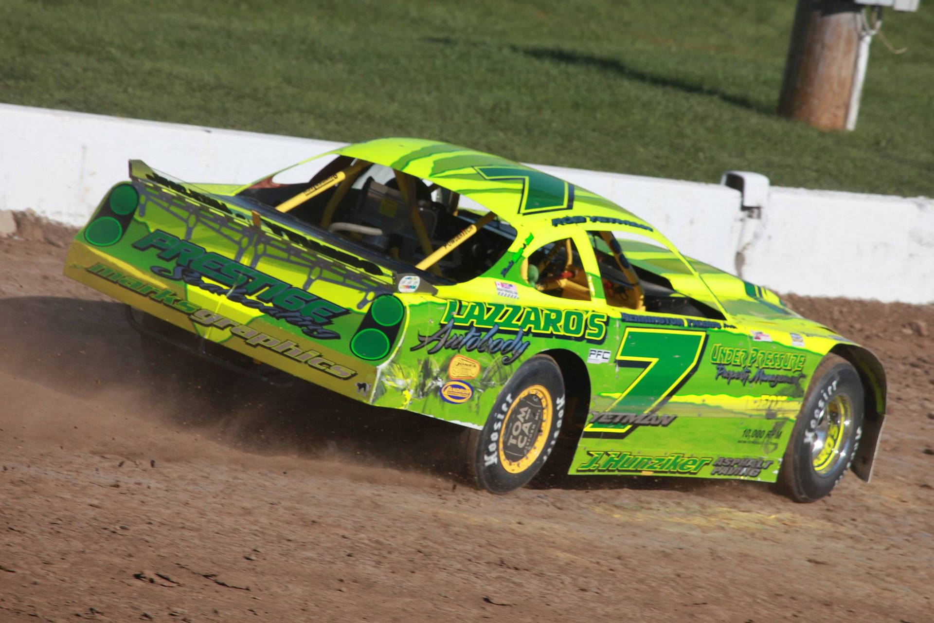 A Green Race Car Driving On A Dirt Track Wallpaper