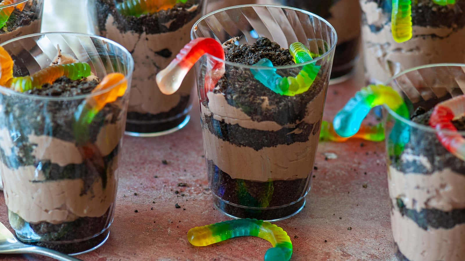 a group of glasses with chocolate pudding and gummy worms