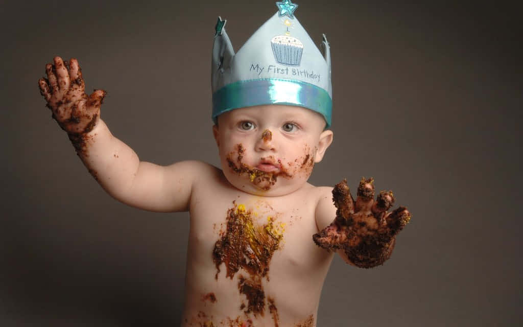 a baby in a muddy t-shirt with a cake hat