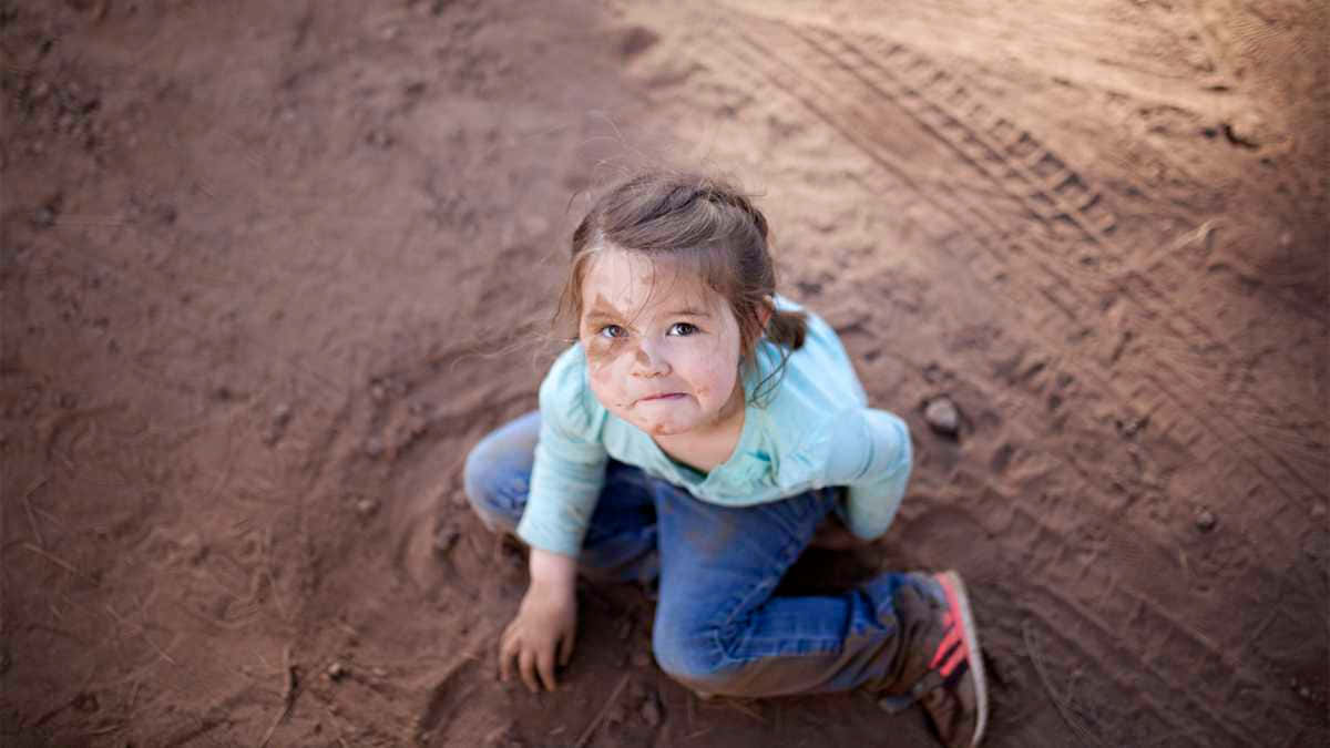A Little Girl Sitting On The Ground In Dirt