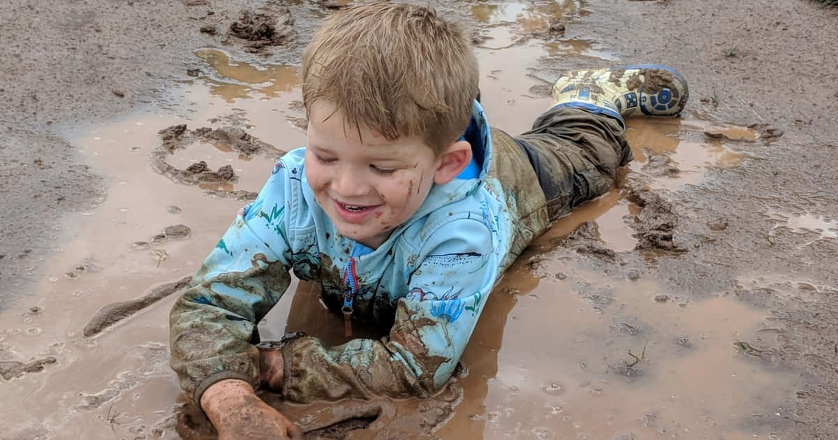 A Young Boy Playing In Mud With A Muddy Puddle