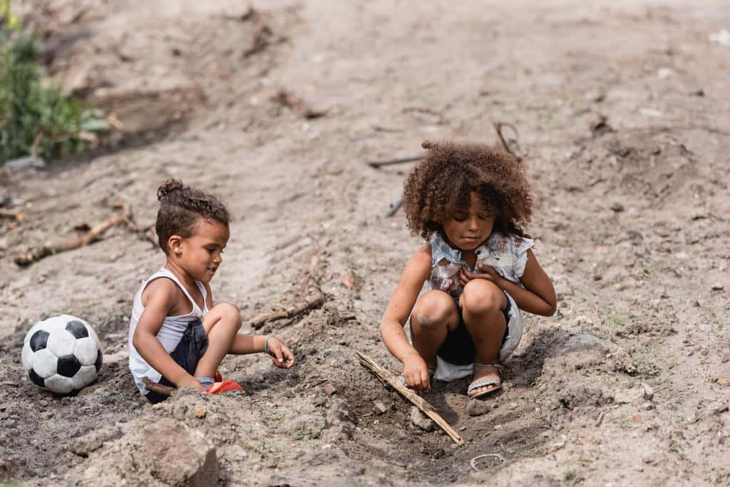 Two Children Playing In The Dirt With A Soccer Ball