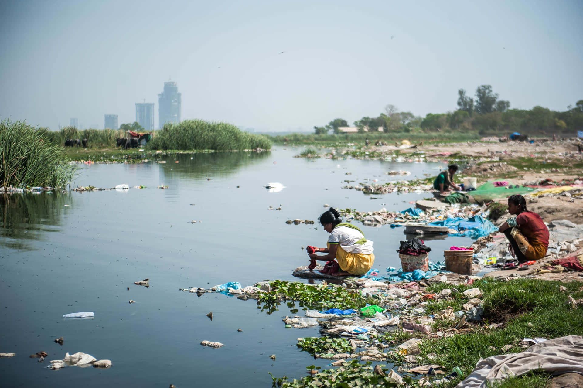 people sitting on the shore of a river with garbage