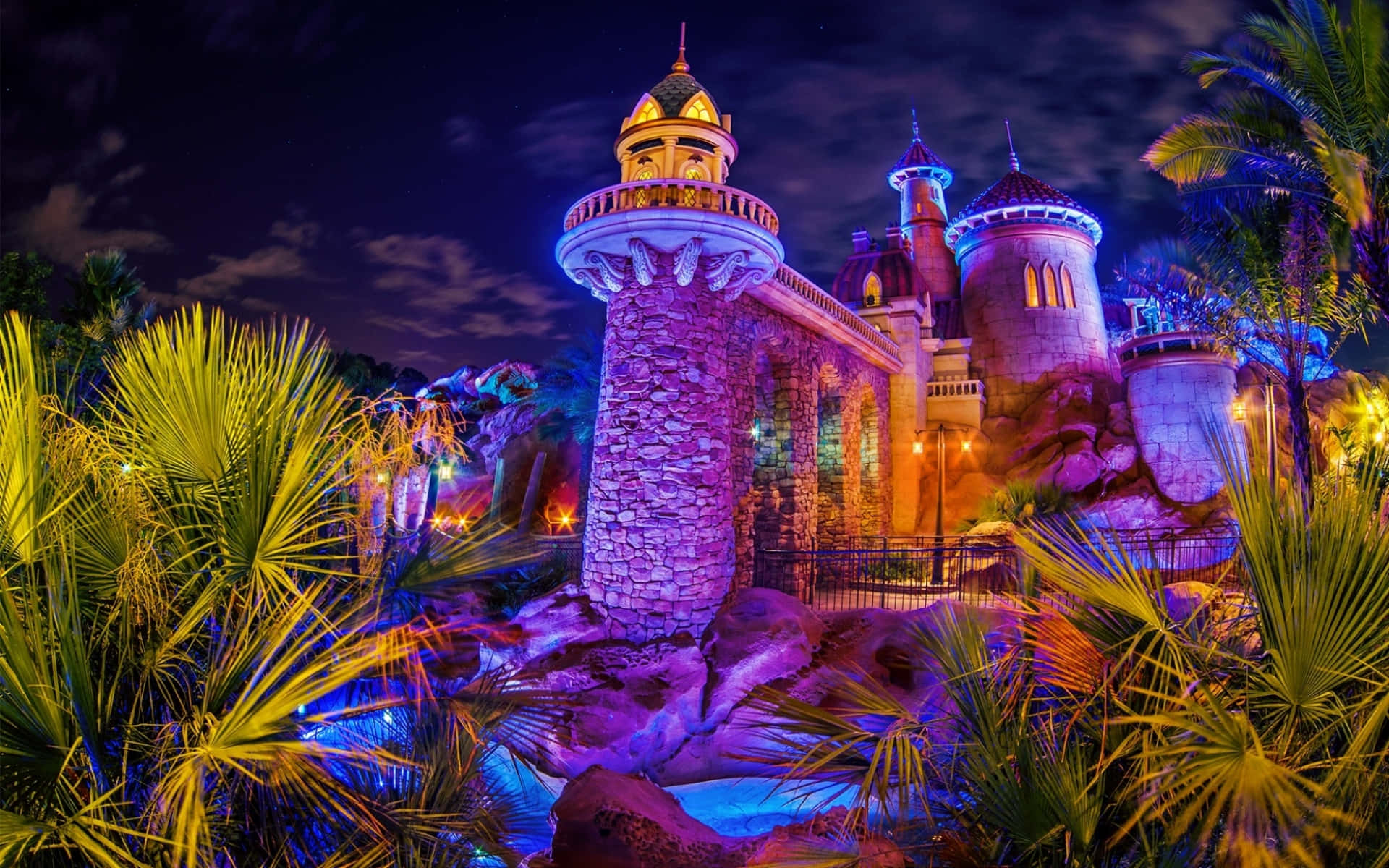 A Castle Lit Up At Night In A Tropical Setting