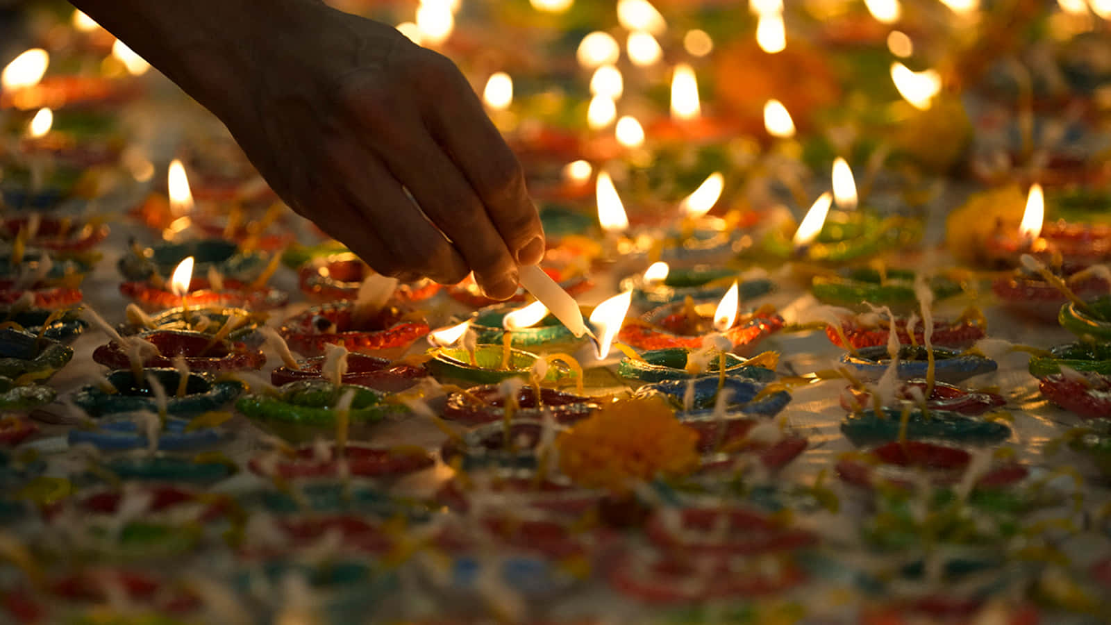 A Person Lighting A Candle On A Table Of Lit Candles