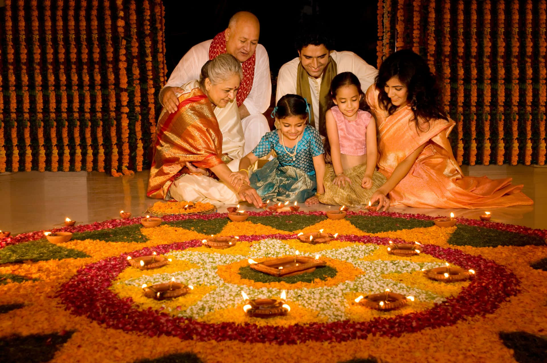 Family Lighting Diyas In Front Of A Flower Arrangement