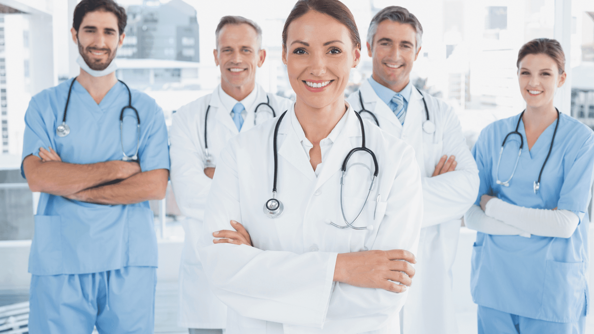 a group of doctors standing together Background — A confident team of smiling medical professionals in scrubs and lab coats stand together with stethoscopes in a bright modern hospital setting.