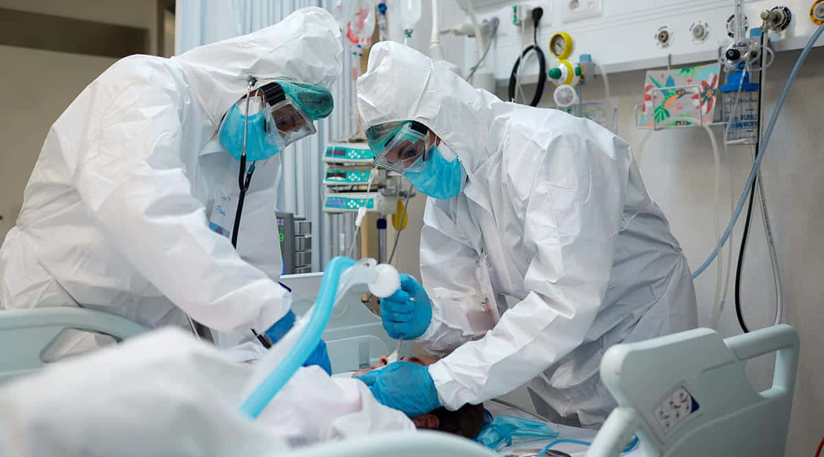 Two People In Protective Suits Are Working On A Patient