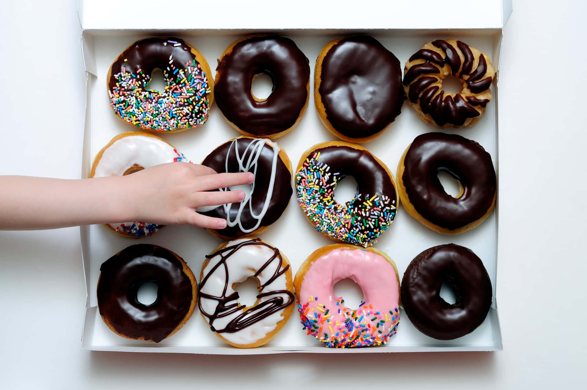 A Child Is Reaching Into A Box Of Donuts