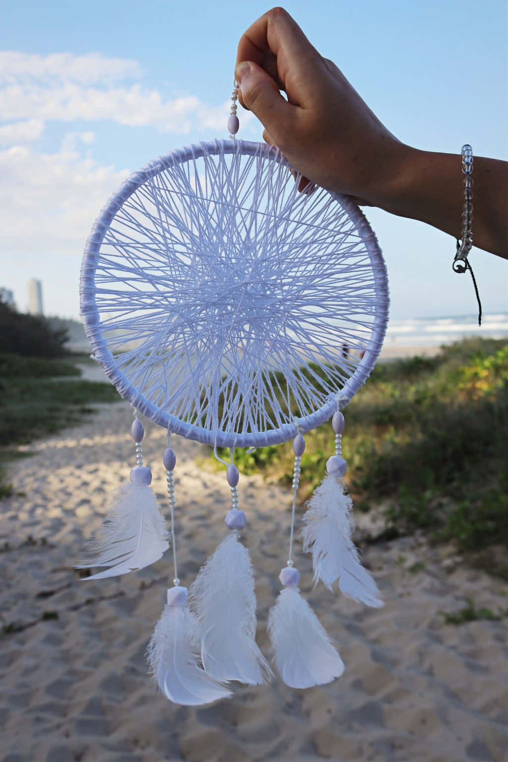 A Person Holding A White Dream Catcher On The Beach