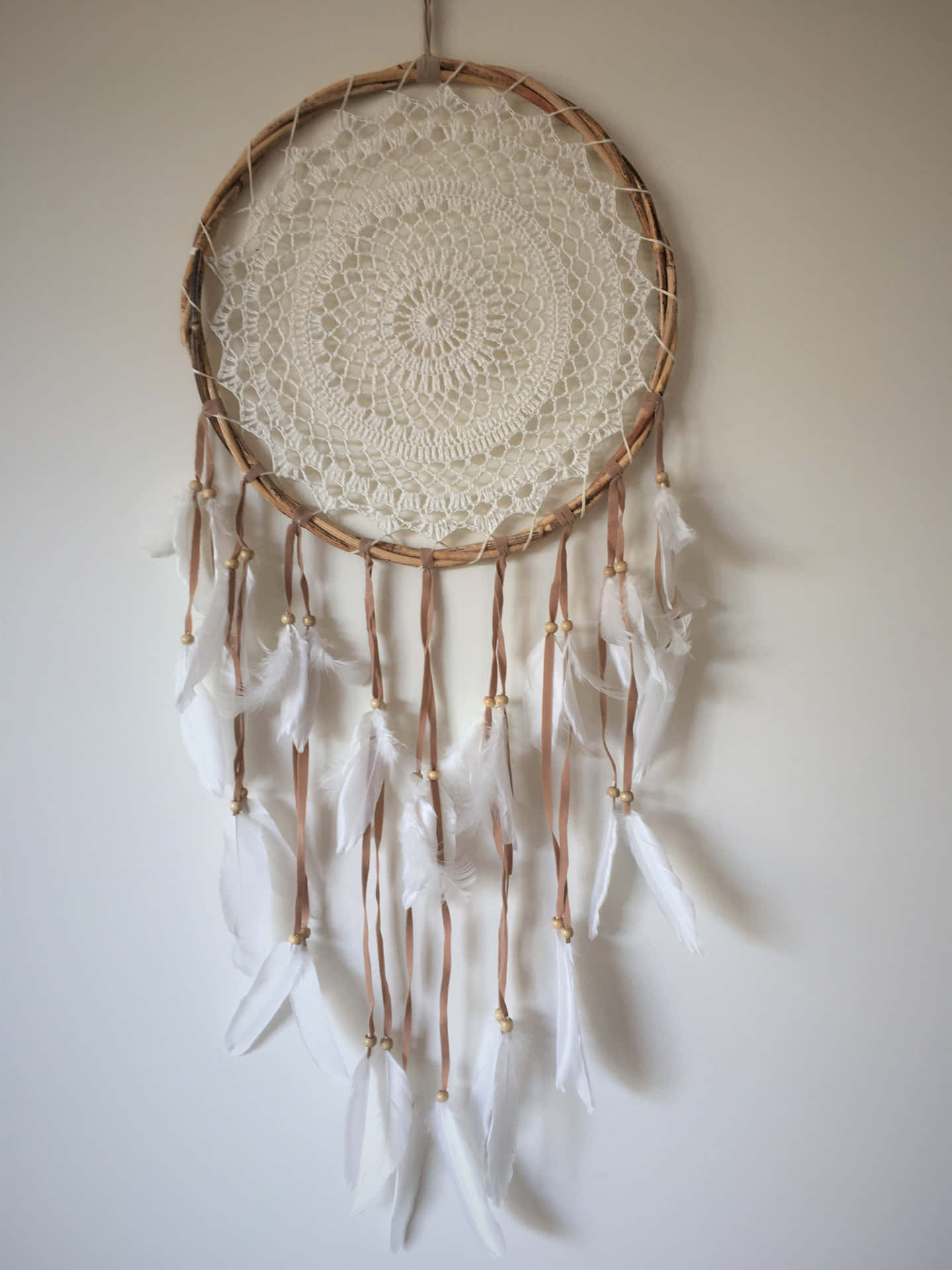 A White Dream Catcher With Feathers Hanging On The Wall