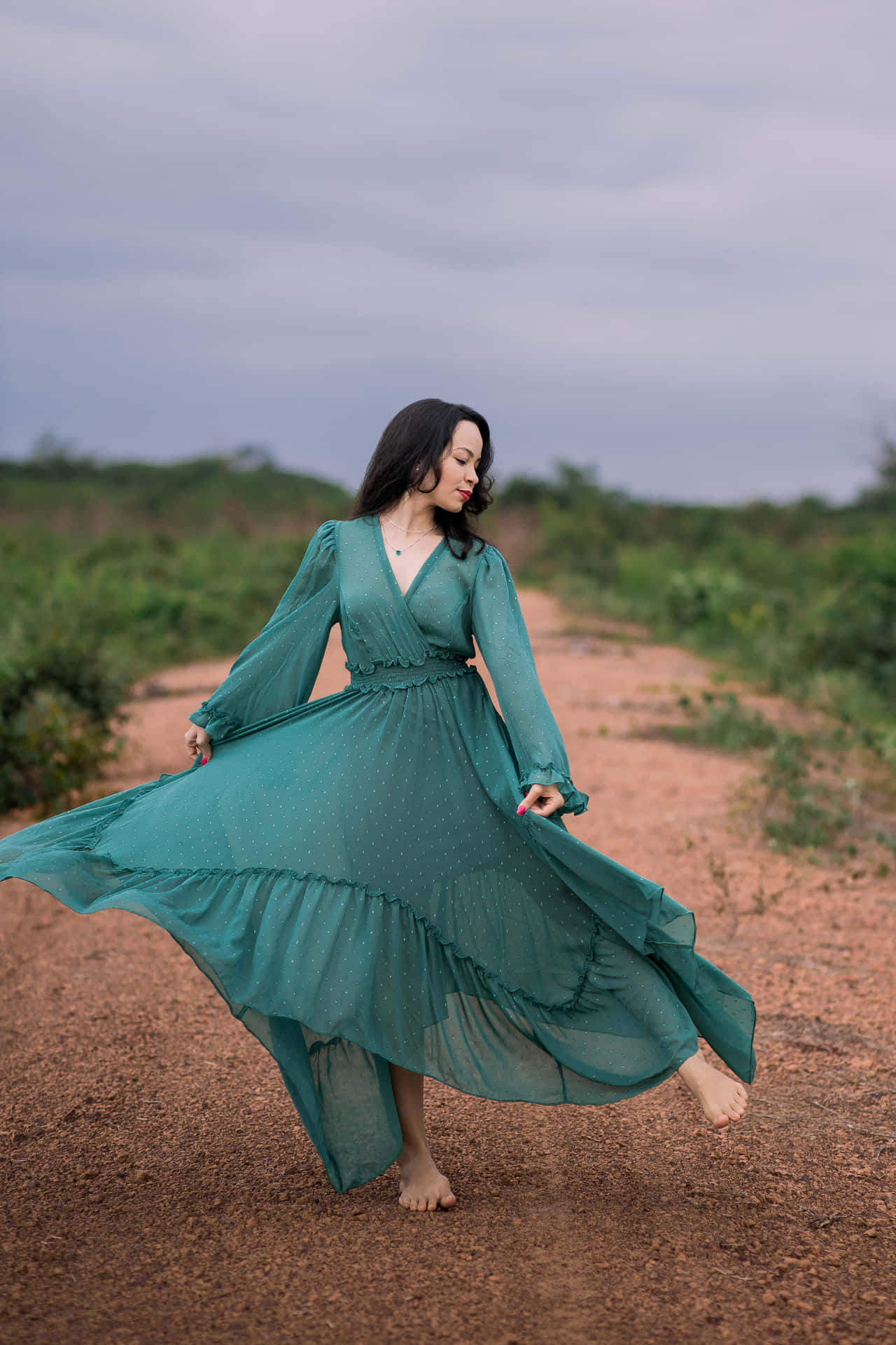 A Woman In A Green Dress Is Dancing On A Dirt Road